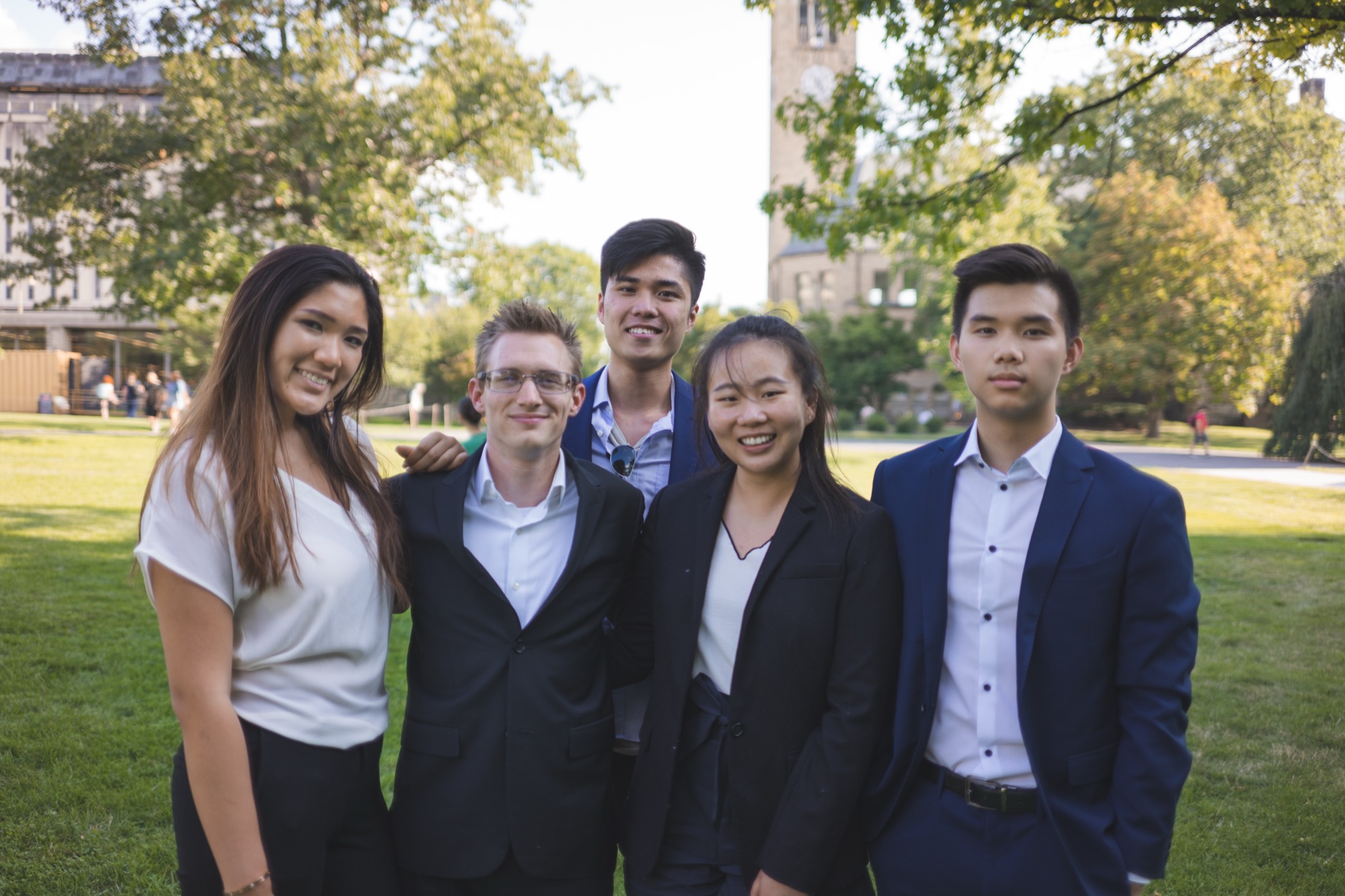 Five members standing together on the Arts Quad with McGraw Tower behind them