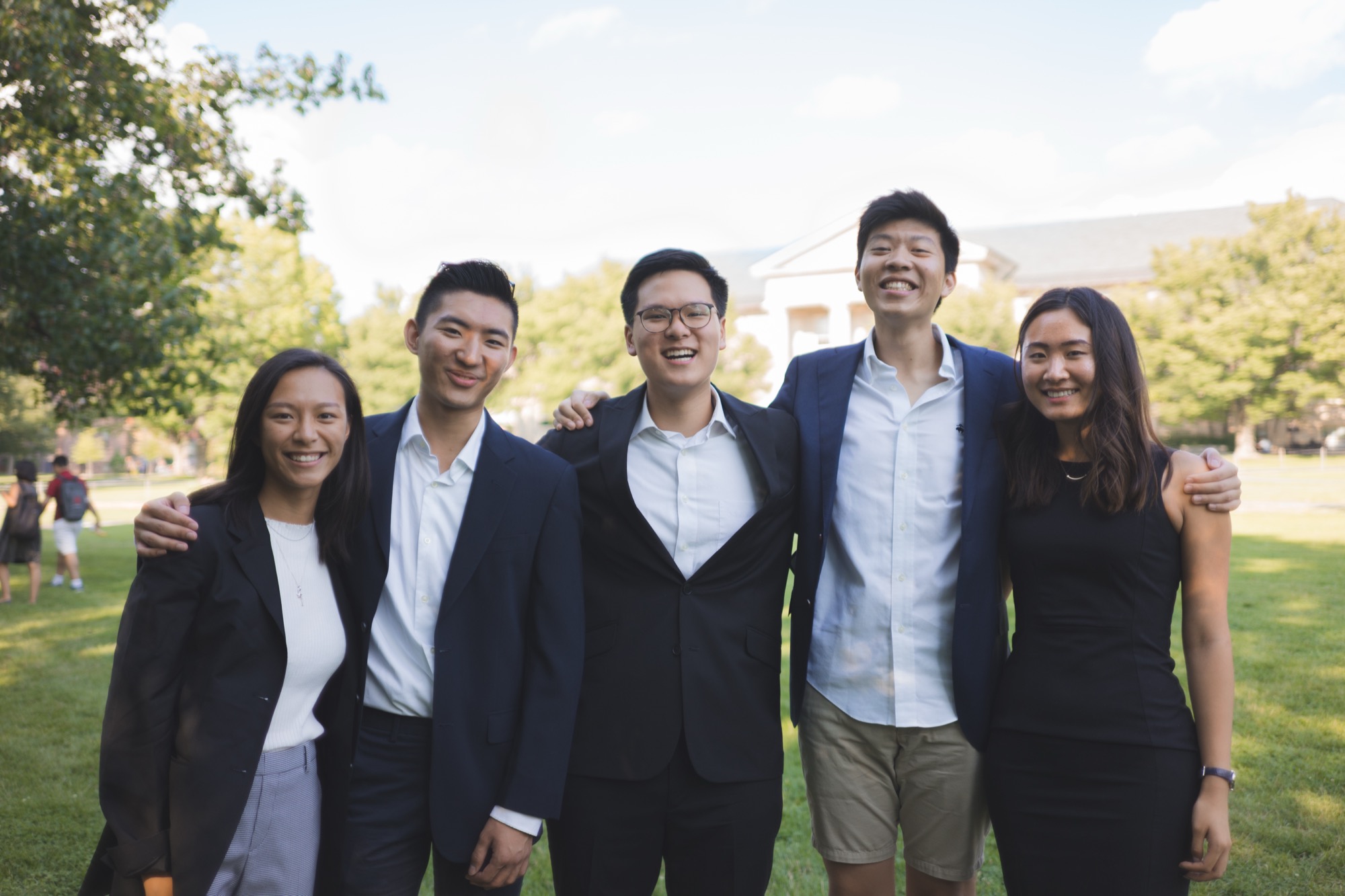 Five members laughing together on the Arts Quad, arms around each other's shoulders