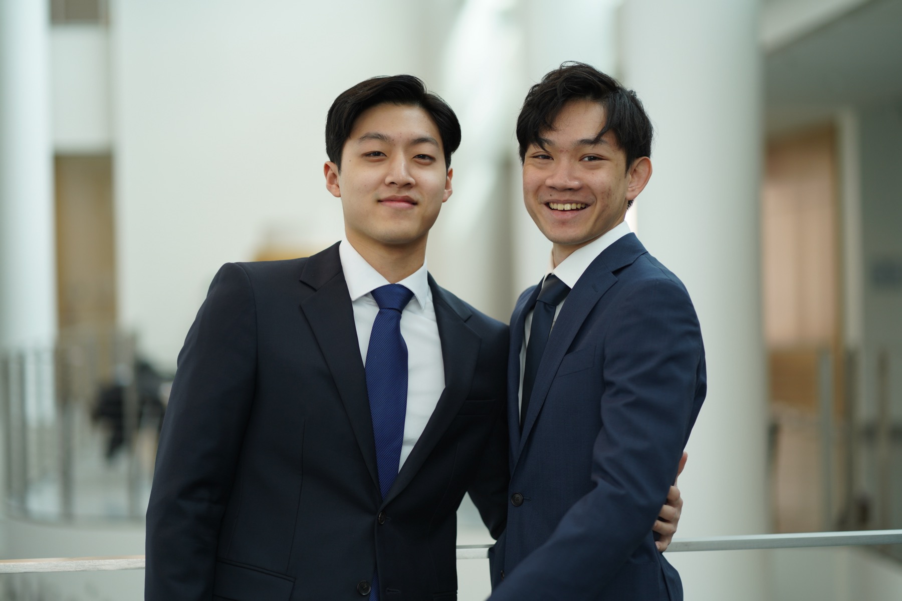 Two members, one laughing, arms around each other's shoulders in the Sage Hall atrium